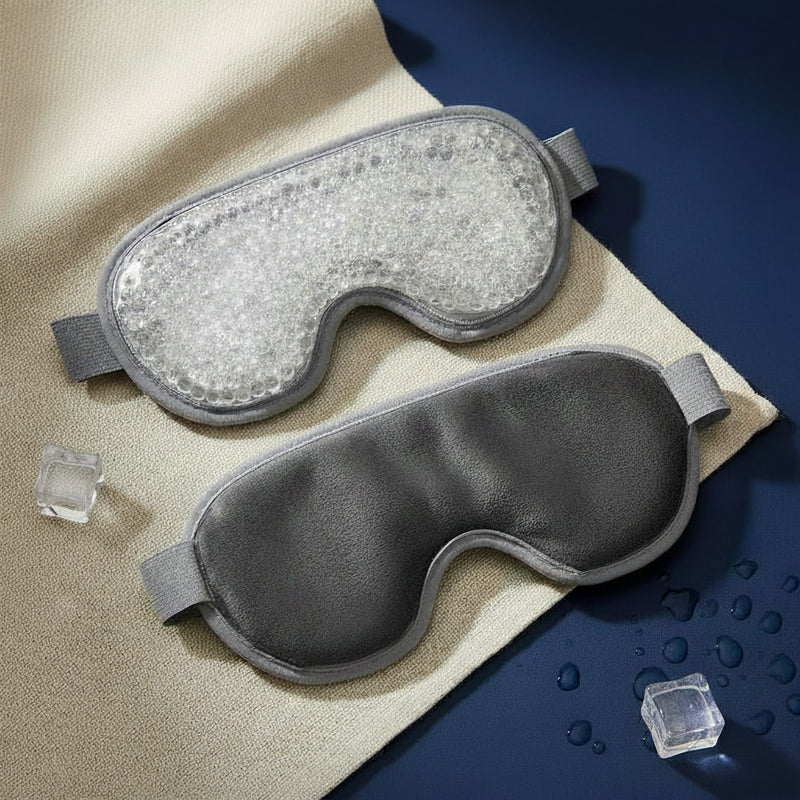 Two cooling eye masks are displayed on a beige textured cloth with ice cubes and water droplets. One mask has a clear bubble gel pad, and the other is dark gray with a smooth texture.